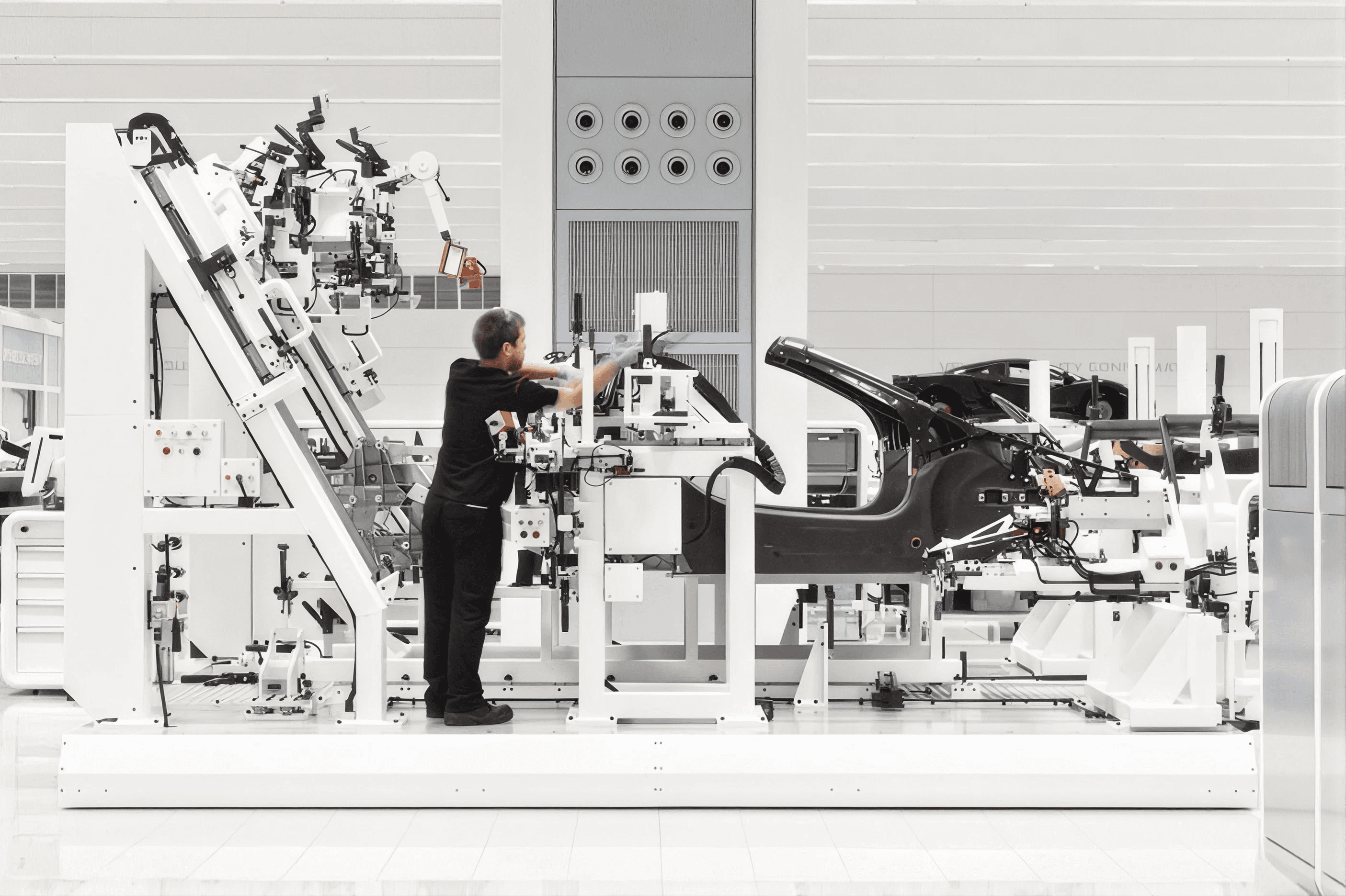 Technician working at a robotic assembly cell around a carbon-fibre car body